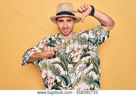 Young handsome man with blue eyes on vacation wearing summer florar shirt and hat smiling making frame with hands and fingers with happy face. Creativity and photography concept.
