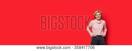 Charming Caucasian Woman Posing On A Red Wall With Free Space Holding Hands In Pocket