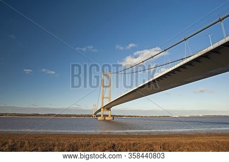 Large Suspension Bridge Spanning A Wide River Estuary On A Clear Day With Blue Sky And Clouds