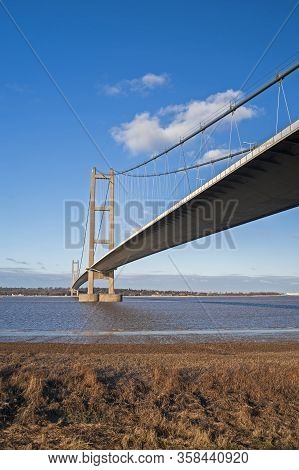 Large Suspension Bridge Spanning A Wide River Estuary On A Clear Day With Blue Sky And Clouds