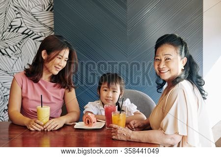 Vietnamese Mother And Grandmother Overindulging Cute Little Girl, Giving Her Tasty Fruit Cocktails A
