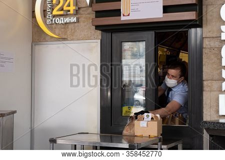 Kiev, Ukraine, 27 March 2020, Man In Facial Protective Mask Gives Fastfood Hamburgers Thru Window At