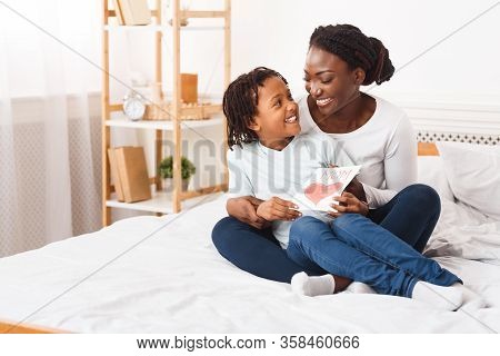 Congatulations. Happy African Mom Embracing Her Little Child And Holding Greeting Card, Sitting On B