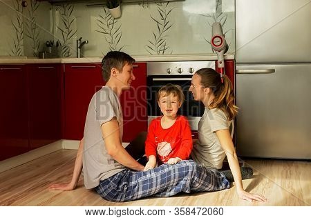 Caucasian Happy Family Sit On The Floor In Kitchen After Cleaning. Gray And Red Colors. Lifestyle, S