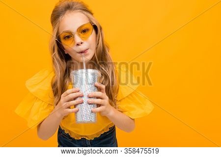 Portrait Of Young Caucaian Girl With Long Fair Hair In Yellow Glasses Drinks A Juice And Smiles