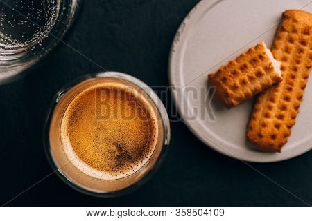 One Portion Of Espresso In Glass Transparent Cups, Bisuits And Water On A Dark Stone Background