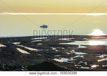 The Pebble Beach Of The Polar Island At Sunset, Far Away From The Shore, The Research Vessel Of A Sc