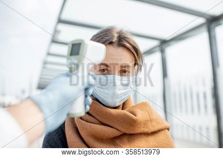 Measuring Temperature With Infrared Thermometer Of A Young Woman In Face Mask At A Checkpoint During