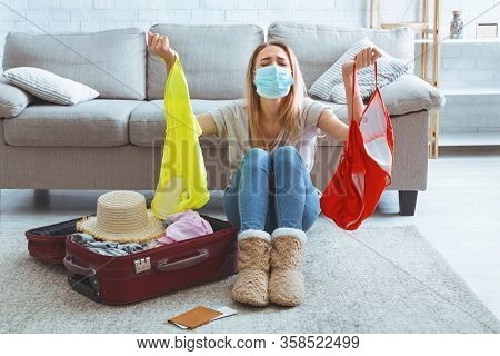 Cancellation Vacation. Saddened Girl In Mask Holds Swimsuits In Hands