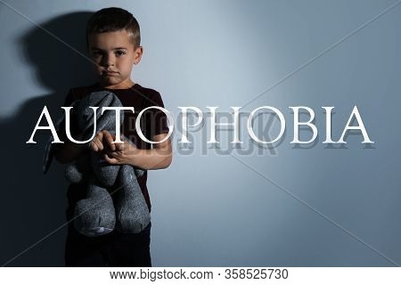Sad Little Boy With Toy Near Light Wall. Autophobia