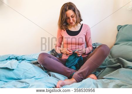Woman Crochets Sitting In Bed, Needlework During Quarantine, The Girl Knits From Thick Blue Yarn, Fe