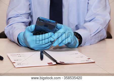 Businessman In Blue Shirt And Tie In Rubber Disposable Gloves With Smartphone.