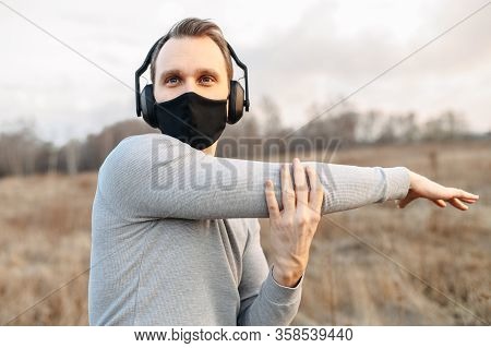Protect Yourself During A Pandemic. Sports In A Medical Mask. Young Atletic Guy In Headphones Doing 