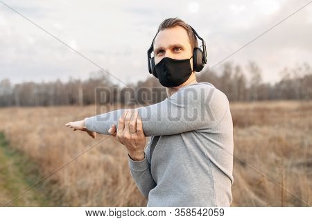Protect Yourself During A Pandemic. Sports In A Medical Mask. Young Atletic Guy In Headphones Doing 
