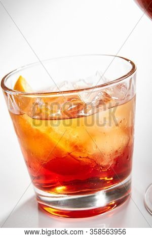 Negroni cocktail close up. Alcohol strong aperitif drink in glass side view. Beverage with red vermouth, Campari liqueur, gin, orange and ice in drinkware. Italian cocktail portion in glassware