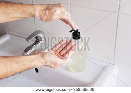 Man Cleaning His Hands Using Liquid Disinfectant Soap And Water In Bathroom.
