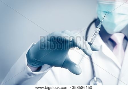 Doctor In Gauze Mask And Medical Robe Holding Syringe In His Blue Rubber Glove Dressed Hand. Health 