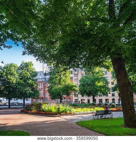 Finnish City Park In Kallio District Of Helsinki, Finland. People Resting On Bench And Walking In Su