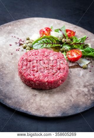 Gourmet tartar raw from beef fillet with lettuce, tomatoes and parmesan with capers as closeup on a rustic modern design plate with copy space 