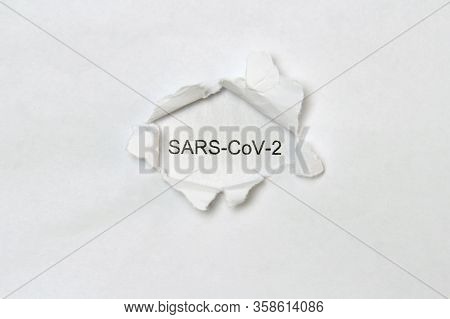 The Word Sars-cov-2 Printed In Black Letters On A White Sheet Of Paper Is Visible In A Hole Torn In 