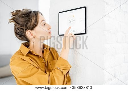 Young Woman Controlling Temperature In The Living Room With A Digital Touch Screen Panel. Concept Of