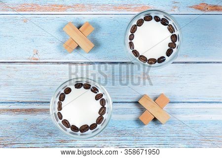 Noughts And Crosses From Glasses With Milk And Beans Of Coffee, Small Wooden Blocks On Light Blue Wo