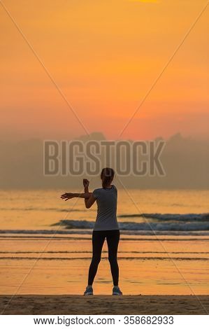Good Shape Woman Standing And Exercise On Beanch In The Morning With Colorful Sky In Background.