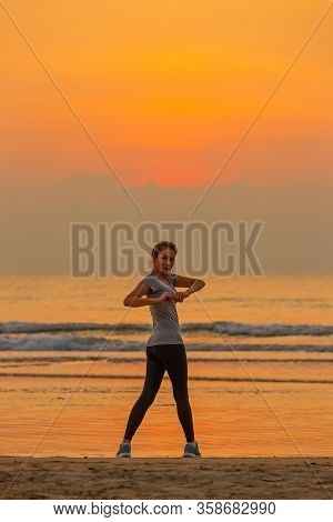 Good Shape Woman Standing And Exercise On Beanch In The Morning With Colorful Sky In Background.
