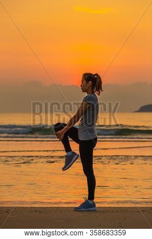 Woman Standing And Exercise On Beanch In The Morning With Colorful Sky And Wave In Background.