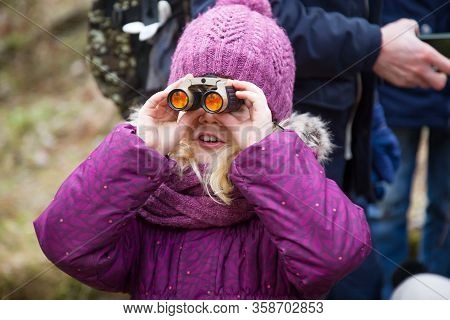 Closeup View Of Small Caucasian Girl Wearing A Purple Hat And Purple Coat Looking Through Binoculars