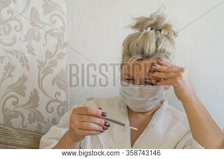 Sick Woman In Bed In Medical Mask Looking At Thermometer With Sadness. Caucasian Middle-aged Woman O