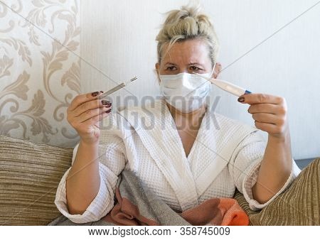 Sick Woman In Medical Mask Looking At Two Thermometers With Sadness. Caucasian Middle-aged Woman On 
