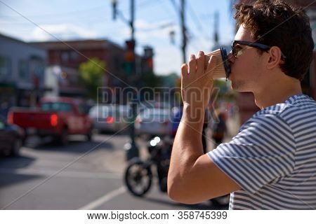 Enjoying City Life. Handsome Young Man In Having Coffee To Go While Magog City In Background, Provin