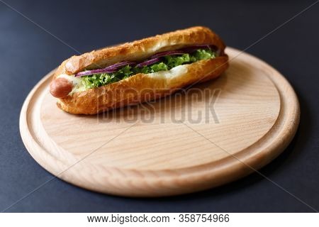 Close Up Of Hot Dog Lying On The Wooden Plate. Fast Food. Isolated Over Black Background.