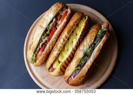 Three Hot Dogs Lying On The Wooden Plate.