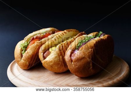Three Hot Dogs Lying On The Wooden Plate.