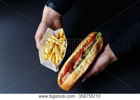 Hot Dog And French Fries In The Hands On The Black Background.