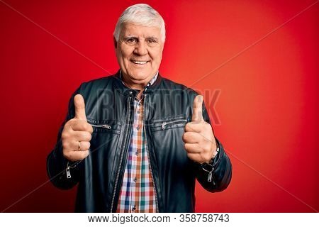 Senior handsome hoary man wearing casual shirt and jacket over isolated red background success sign doing positive gesture with hand, thumbs up smiling and happy. Cheerful expression and winner