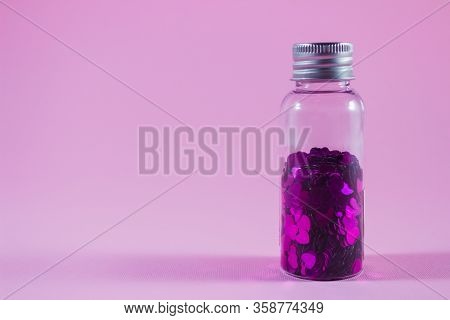 Glass Bottle With Purple Heart Shaped Sparkles On Pink Background