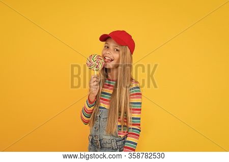 Lollipop Makes Her Happy. Cute Little Girl Eating Rainbow Swirl Candy On Yellow Background. Small Ch