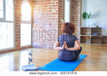Middle age beautiful sportwoman sitting on mat on backview practicing yoga doing reverse prayer pose at gym