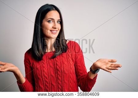 Young brunette woman with blue eyes wearing casual sweater over isolated white background smiling showing both hands open palms, presenting and advertising comparison and balance