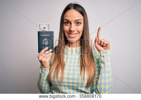 Young blonde tourist woman holding id passport with dollar as money for vacation surprised with an idea or question pointing finger with happy face, number one