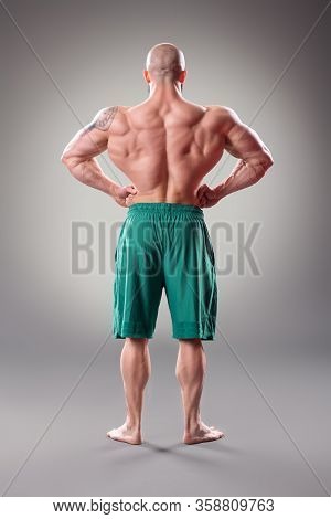 Sexy Muscular Bodybuider Posing On The Gray Background. Back View