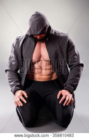 Sexy Muscular Bodybuider Posing With Sweatshirt And Hood On The Gray Background