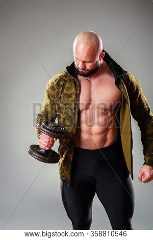 Sexy Muscular Bodybuider Posing With Sweatshirt And Lifting Weights On The Gray Background.