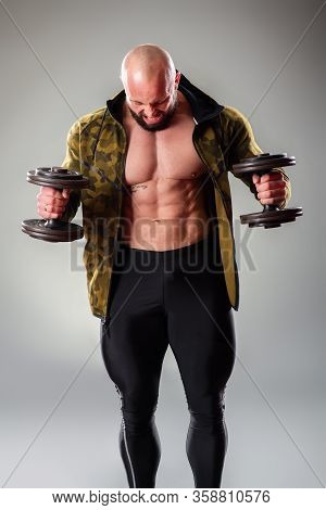 Sexy Muscular Bodybuider Posing With Sweatshirt And Lifting Weights On The Gray Background.