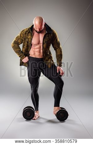 Sexy Muscular Bodybuider Posing With Sweatshirt On The Gray Background.