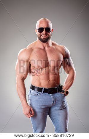 Sexy Muscular Bodybuider With Sunglasses Posing On The Gray Background