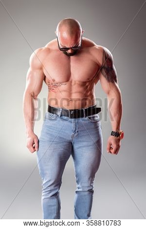 Sexy Muscular Bodybuider With Sunglasses Posing On The Gray Background